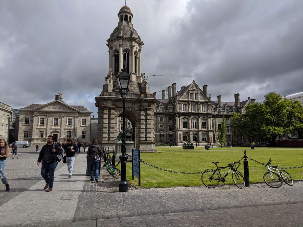 Image from the Trinity College Dublin courtyard. Beautiful old buildings are surrounding it and in the middle of the yard, there is green grass.