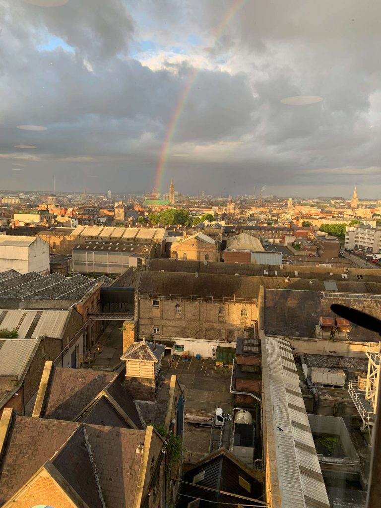 Dublin rooftops which of some are hit by a rainbow dropping from a cloudy sky.