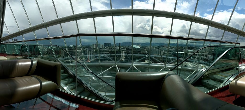 An ill-dimensioned panorama photo portraying the view from inside of the Convention Centre Dublin with brown couches in the foreground.